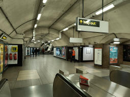 At the top of the escalators from the westbound platform, the eastbound is on the right and the escalators up to the ticket hall are ahead